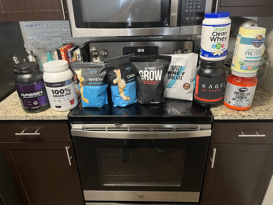 Different types of the best protein powder we’ve tested at Garage Gym Reviews in our testing facility are spread over a stove and the surrounding countertops